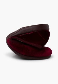 Zapatilla de terciopelo burdeos con forma redondeada y un talón acolchado. Presenta una suela flexible y un detalle de cuero suave. No contiene herrajes visibles.