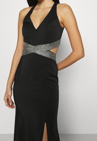 Černé večerní šaty s hlubokým výstřihem do V, vykrojenými stranami a korálkovým opaskem, s úzkým střihem a bočním rozparkem.