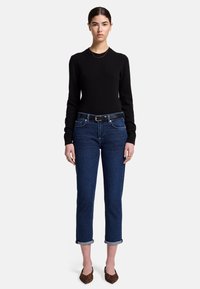 Maglione nero a maniche lunghe, jeans blu scuro con orli risvoltati, cintura nera e ballerine marroni con motivo. Design semplice con texture morbide.