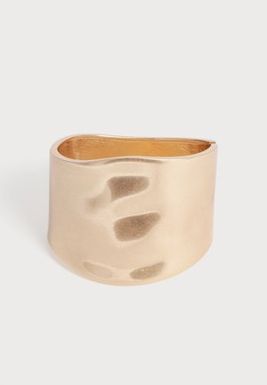 Ampio bracciale a polsino in oro con superficie liscia, leggermente irregolare e design posteriore aperto.