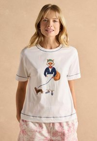 Valge puuvillane T-särk lühikeste varrukatega, millel on illustreeritud rebane sinises ülikonnas, kes jalutab koera rihma otsas, aktsentidega sinise õmblusega.