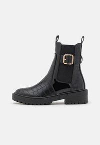 Botas negras hasta el tobillo con un patrón texturizado de cocodrilo y acentos brillantes. Presenta una hebilla dorada, paneles laterales elásticos y una suela gruesa.