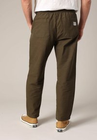 Homme portant un pantalon décontracté vert olive avec taille élastique et poches arrière, associé à des baskets montantes marron clair.