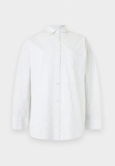 Chemise blanche à manches longues avec des rayures verticales subtiles et une poche poitrine unique, présentée sur un fond uni.