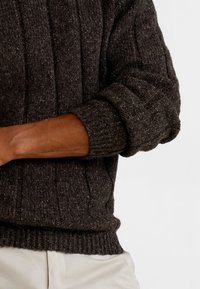 Pull en maille gris foncé avec côtes verticales, tissu texturé et manches retroussées. Dispose d'un ourlet ajusté à la taille.