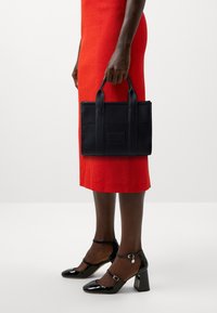 Sac cabas en cuir noir à surface texturée, forme rectangulaire et deux poignées ; assorti avec une robe rouge et des talons noirs vernis.