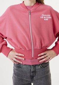 Giacca bomber rosa con zip frontale, polsini e fondo a coste. Presenta la scritta bianca "Garcia I’M ON CLOUD NINE" sul petto. Texture morbida.