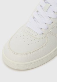 Hvide lædersneakers med tekstureret overflade, der har en glat, rund tå, perforerede detaljer og hvide snørebånd. Gummisålen er synlig.