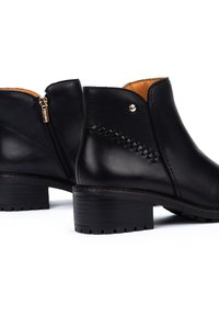 Bottines en cuir noir avec fermeture éclair sur le côté, talon empilé et détails de couture décoratifs sur les côtés. L'intérieur est beige.