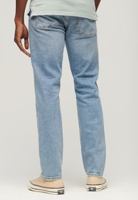 Jasnoniebieskie dżinsy o prostym kroju z dwiema tylnymi kieszeniami i czystym wykończeniem, połączone z beżowymi sneakersami z płótna.