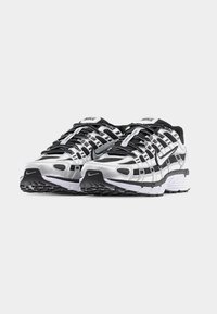 Ζευγάρι από μαύρα, λευκά και ασημί αθλητικά παπούτσια Nike Air για τρέξιμο με πλέγμα και συνθετικά επικαλύμματα, τοποθετημένα δίπλα-δίπλα σε λευκό φόντο.