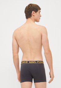 Dunkelgraue Boxershorts für Männer mit einem schwarz-gelben Bund, der den Markennamen trägt. Glattes Material, enganpassendes Design mit Nahtdetails.
