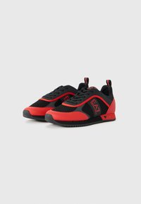 Black and red sneakers featuring a mesh upper, rubber sole, and textured accents. Logo displayed on the side and tongue.