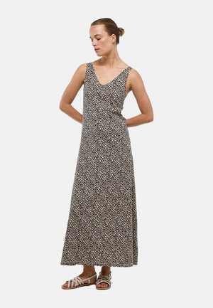 Femme portant une robe sans manches longue jusqu'aux chevilles à imprimé léopard et des sandales beiges à brides, debout avec les mains dans le dos.