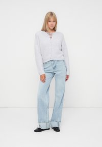 Ljusgrå kort cardigan med knappar, bärs över en röd- och vitrandig topp, parat med ljusblå vida jeans. Svarta skor.