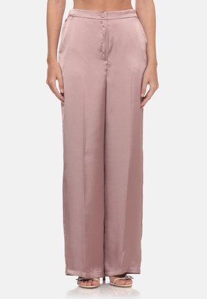 Donna che indossa pantaloni in raso a vita alta con gamba larga color rosa polveroso con tasche laterali e chiusura con bottoni, abbinati a sandali open toe.