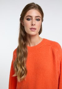 Maglione lavorato a maglia in vivace arancione con collo tondo, polsini a coste e vestibilità ampia. Tessuto morbido e design leggermente oversize.