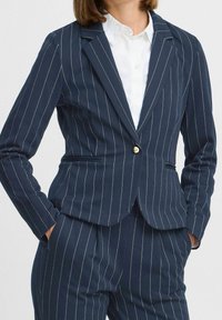 Granatowa marynarka w prążki z gładkiej tkaniny, z pojedynczym złotym guzikiem, klapami z nacięciem i kieszeniami z patkami, dopasowany krój.