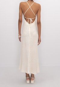 Robe maxi crème à motifs léopard avec un dos nu, des bretelles spaghetti et un lien ajustable. Tissu lisse et fluide avec un léger éclat.