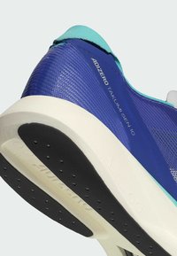 Zapatilla deportiva azul y turquesa con parte superior texturizada, entresuela blanca y suela de goma negra con patrones de tracción circulares.