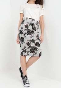 Jupe crayon grise avec un motif de feuilles tropicales noires et roses, associée à une chemise blanche et des baskets montantes noires.