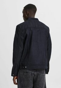 Chaqueta de ante azul oscuro con una textura suave, que presenta un cuello alto, costuras en los hombros y cierres a presión en la cintura.