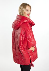 Rød puffjakke med en stor hætte, quiltet design, glat tekstur, sidelommer og justerbar snøre i bunden.