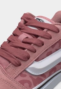 Κοντινό πλάνο ροζ αθλητικού παπουτσιού με υφασμάτινα κορδόνια, σουέτ λεπτομέρειες, λευκή πλευρική ρίγα και τμήμα υφάσματος με λεοπάρ σχέδιο.