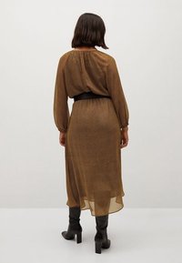 Brązowa sukienka w kropki, długa, z podkreśloną talią i balonowymi rękawami. Przezroczysty materiał sięga do połowy łydki, w połączeniu z czarnymi kozakami do kolan.