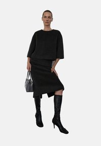 Suéter negro corto y falda de tela texturizada, combinados con botas negras hasta la rodilla. Bolso gris con dos asas.