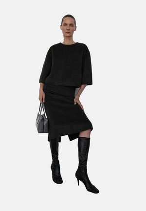 Suéter negro corto y falda de tela texturizada, combinados con botas negras hasta la rodilla. Bolso gris con dos asas.