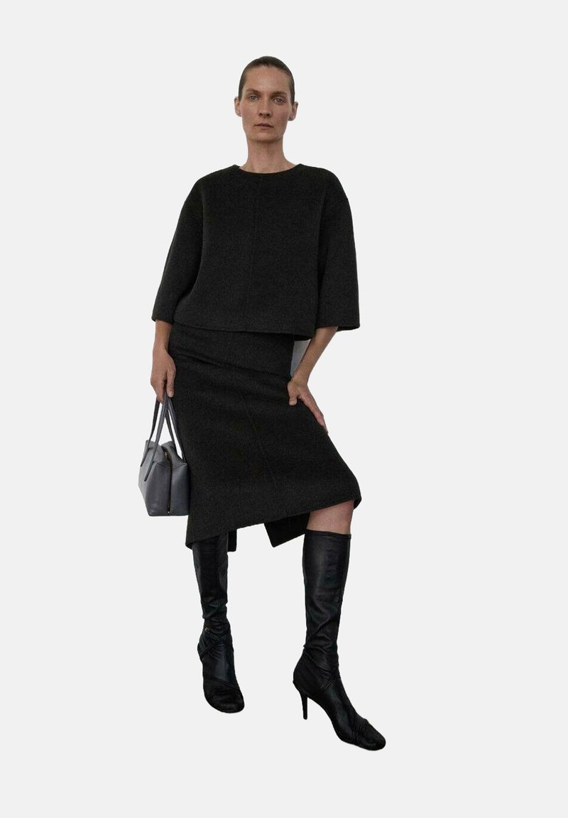 Suéter negro corto y falda de tela texturizada, combinados con botas negras hasta la rodilla. Bolso gris con dos asas.