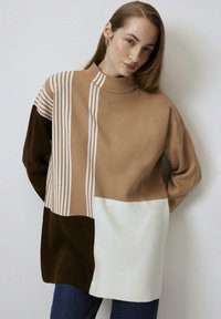 Oversized trui met een beige, bruine en witte kleurblokontwerp, verticale strepen en een hoge hals. Zachte gebreide textuur.
