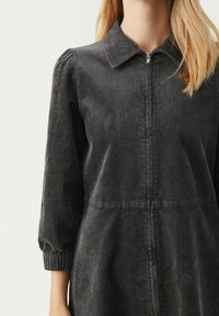 Dunkelgraues Cordkleid mit einem Kragen, einem durchgehenden Reißverschluss und dreiviertellangen Ärmeln mit gerafften Manschetten. Vertikale Rippstruktur ist deutlich sichtbar.