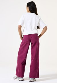 Pantalones anchos color marrón oscuro combinados con una camiseta blanca de manga corta, con un corte casual y bolsillos traseros estándar.