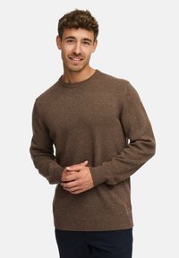 Brązowy sweter dzianinowy z okrągłym dekoltem oraz ściągaczami przy mankietach i na dole. Materiał jest miękki i teksturowany. Logo marki jest widoczne w lewym dolnym rogu.