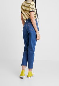 Högmidjade blå denimjeans med avslappnad passform, stylade med en randig gul och svart skjorta och gula hög-tops sneakers.