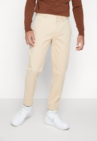 Beżowe bawełniane spodnie o prostym kroju, z zapięciem na guzik, szlufkami na pasek i bocznymi kieszeniami, zestawione z białymi trampkami.