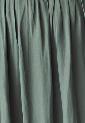 Tissu plissé vert avec une texture lisse. Le matériau présente un léger éclat et se drape doucement, créant des plis délicats.