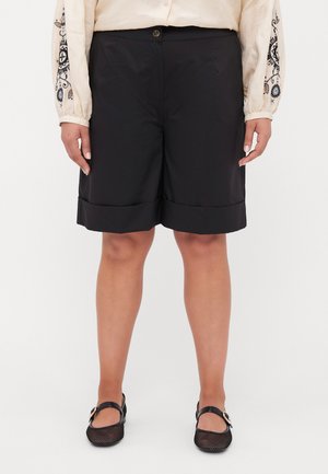 Black shorts made of lightweight fabric, featuring a folded hem and side pockets. Worn with a light-colored, long-sleeve shirt.