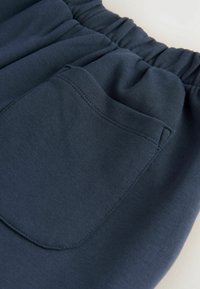 Pantaloni din bumbac bleumarin, cu un amestec de fibre, prevăzuți cu un cintura elastică și un buzunar tip patch cu cusături întărite pe lateral. Textură moale, design lejer.