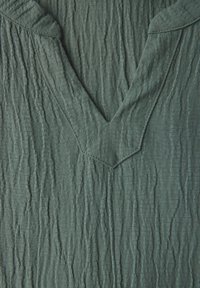 Skrynklig teal-färgad tyg med V-ringning och texturerad yta. Har ett mjukt, lätt skrynkligt utseende med subtil kontrastsöm.