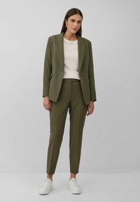 Blazer taillé vert olive avec un pantalon slim assorti, haut texturé blanc et baskets blanches. Lignes épurées et design minimaliste.