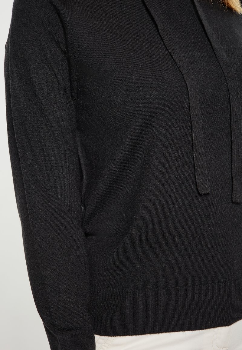 Felpa nera con cappuccio dal tocco morbido, dotata di una tasca frontale e coulisse. Il design è a vestibilità comoda con bordi a costine.