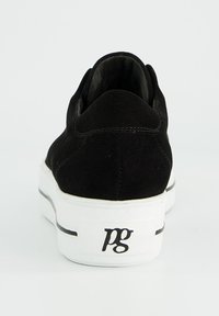 Schwarze Wildleder-Sneaker mit dicker weißer Gummisohle, von hinten betrachtet, mit schwarzem "pg"-Logo auf der Ferse der Sohle.