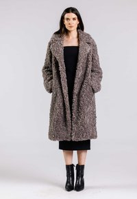 Teddy grå faux shearling jakke med bred krave, åben foran og to sidelommer. Bæres over en tætsiddende sort kjole og ankelstøvler.