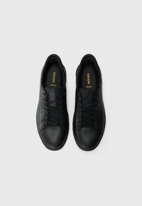 Sorte lærersneakers med en glat tekstur, rund tå og flade snørebånd. Har perforeret indersål og guld "GEOX Respira" branding.