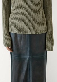 Pull en maille côtelée vert olive à manches longues associé à une jupe en cuir foncé au toucher lisse avec des coutures apparentes.