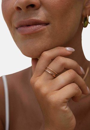 Ringe aus roségold mit einem verdrehten Banddesign und glatten Oberflächen. Sanfter, natürlicher Hautton und sorgfältig manikürte Fingernägel mit heller Nagellackierung.