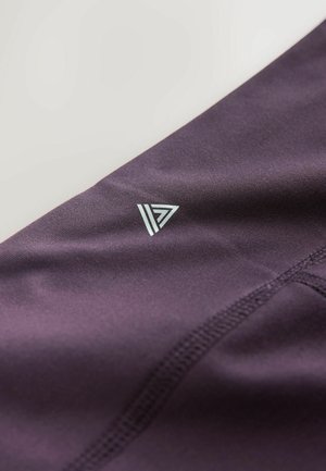 Violets sporta audums ar gludu tekstūru ar gaisīgi zilu trīsstūra formu logotipu, kas novietots netālu no šuves.